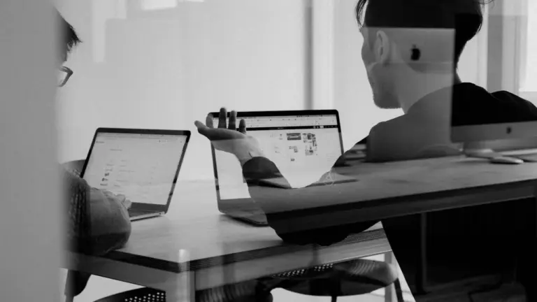 Two colleagues discussing work at laptops