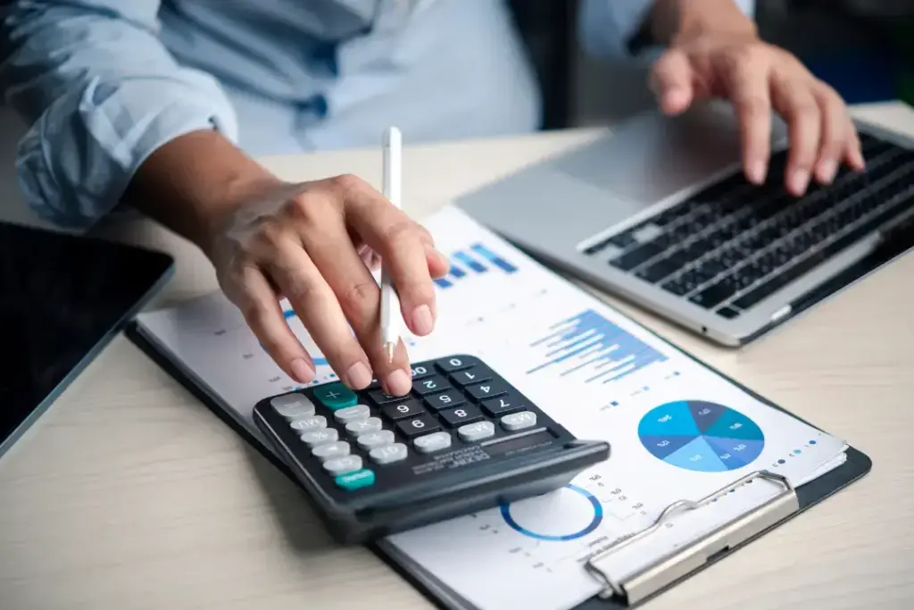 Person using calculator and laptop for financial analysis.