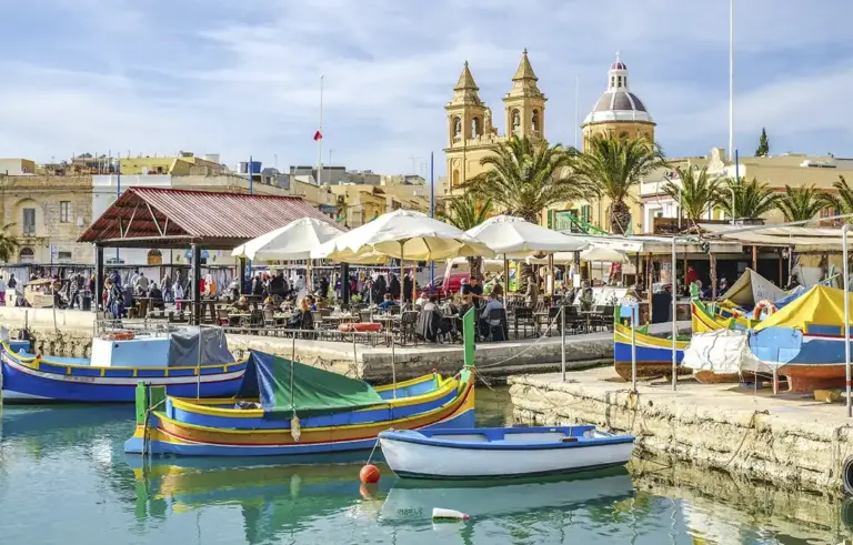 Colourful boats in Maltese waterfront village scene.